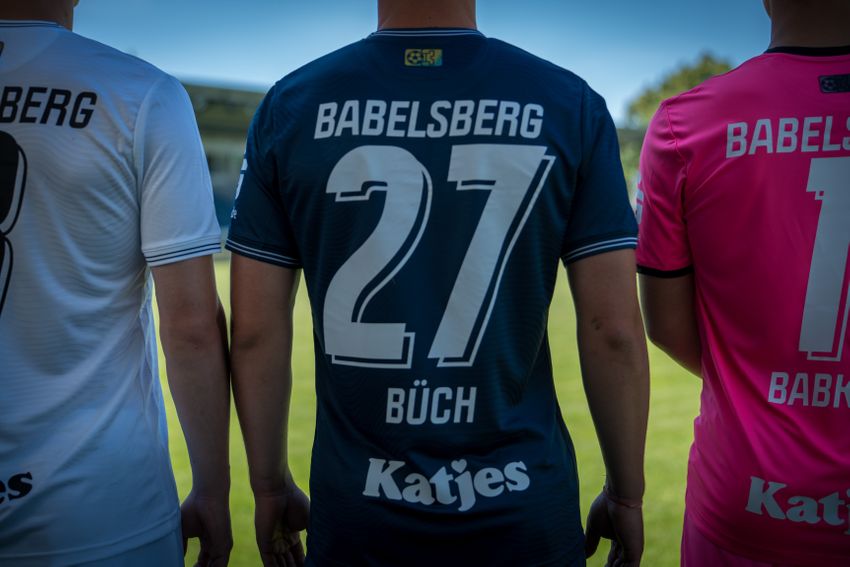 Angeschnittes Bild mit den Rückenansichten der weißen, blauen und pinken Trikots. Im Fokus der Rücken von Gordon Büch und seiner 27.
